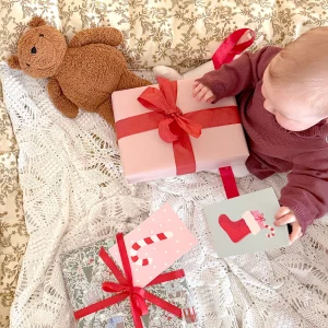 Baby som sitter och tittar på julklappar med röda rosetter och julkort på.