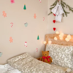Väggdekoration med julmotiv ovanför en säng med granris och ljus hängande över.