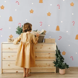 Väggdekoration med julmotiv av pepparkakor formade som julgranar och stjärnor samt polkagrisar, med en liten flicka i klänning som står framför en byrå.