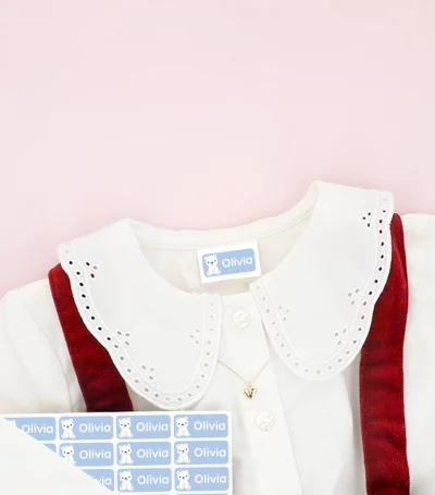 Barnskor och barnklänning med namnlappar fästa på kläderna, omgivna av snöflingedekorationer.