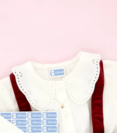 Barnskor och barnklänning med namnlappar fästa på kläderna, omgivna av snöflingedekorationer.