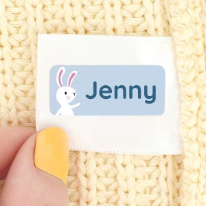 Personlig navnelapp med navnet Jenny og en søt kaninillustrasjon, festet på en gul strikket genser. Perfekt for å merke klær og eiendeler for barn.