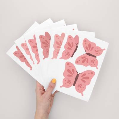 Hand som håller ark med väggklistermärken med blå fjärilsdesign, perfekt för barnrum.