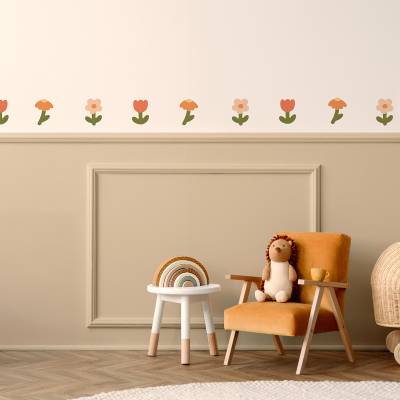 Väggdekor med blomsterdesign i mjuka färger på väggen ovanför en mysig stol i ett barnrum.