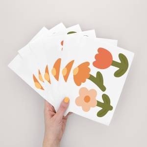 Hand som håller en bunt väggdekorer med färgglada blomsterdesigner.
