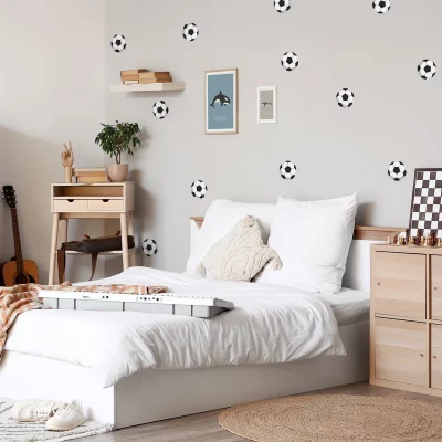 Barnrum med modern väggdekor med fotbollar, en säng med vita sängkläder, en byrå och en gitarr.