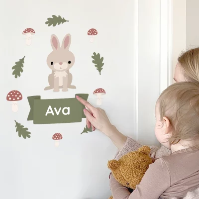 Veggdekor i barnerom med navn 'Ava', illustrert med en søt kanin og naturlige elementer, som passer perfekt for å personliggjøre barnets rom. En mor og hennes barn viser frem dekoren.