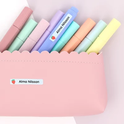 Flera färgglada pennor i en rosa pennfodral med en namnlapp. Namnlappen visar ett namn och en jordgubbsillustration, perfekt för att personalisera skolmaterial eller konstprojekt för barn. Denna produkt, en navnelapp, är idealisk för att hålla ordning på barnens grejer.