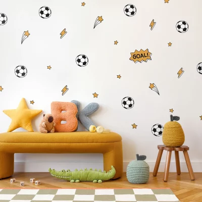 Väggdekor med fotbollstema för barnrum, inkluderar fotbollar, blixtar och stjärnor i färgglada design. En pratbubbla med texten GOAL! pryder väggen. I förgrunden syns en gul soffa med en stjärna, bokstäver i mjukt material, en leksak och korgar. Perfect för att skapa en lekfull och inspirerande miljö för barn.