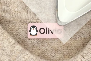 Färggrann navnlabel med en söt pingvin och namnet Olivia, som ligger på en mjuk yta. Perfekt för att personifiera barnets tillhörigheter och ge en lekfull touch. Idealisk för att användas på kläder, väskor och andra föremål.