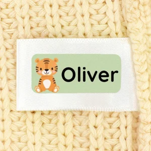Namnlapp med en tiger som motiv och namnet Oliver, placerad på en mjuk, gyllene fleecebakgrund. Perfekt för att ge barnkläder eller tillbehör en personlig touch.
